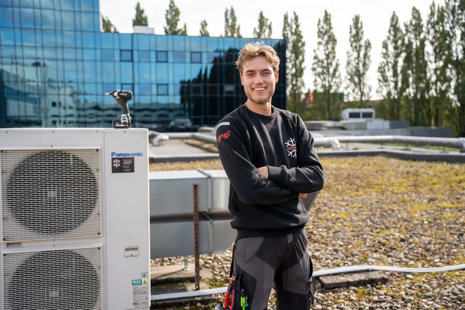 Monteur van Jadikoel met de armen over elkaar naast een airco buitenunit op het dak