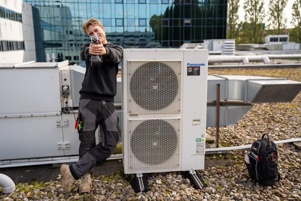 Monteur van Jadikoel bij een airconditioning buitenunit op het dak van een kantoorpand