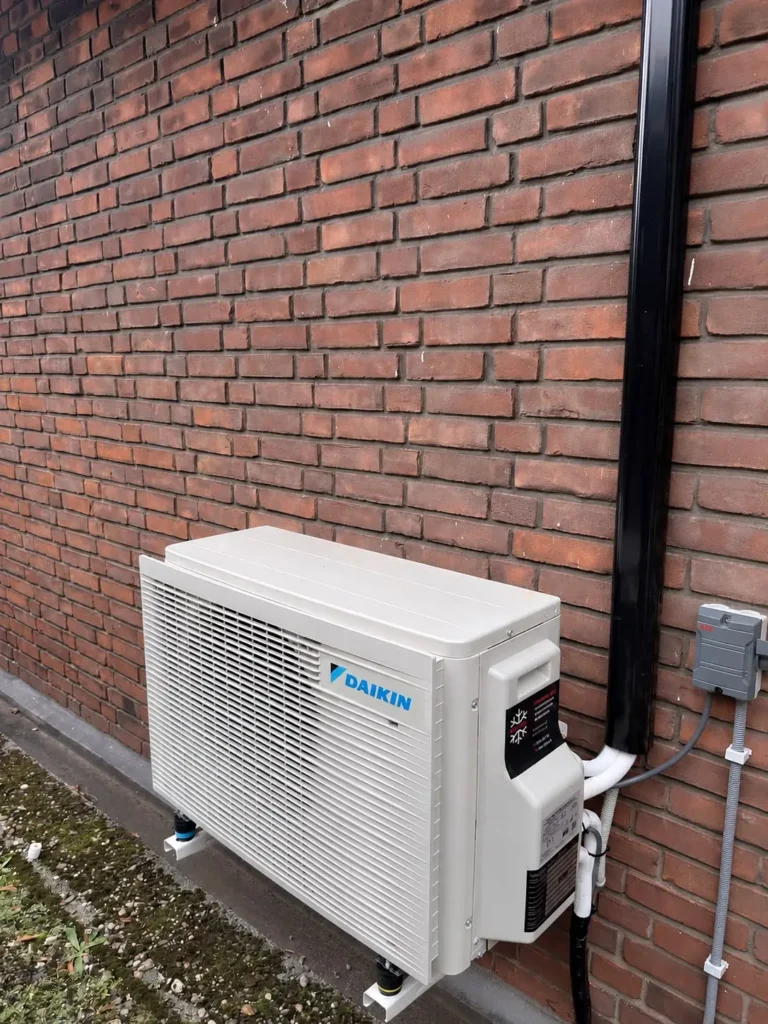 Daikin airco buitenunit aan een bakstenen gevel met nette leidinggoot, geplaatst door Jadikoel in Voorburg